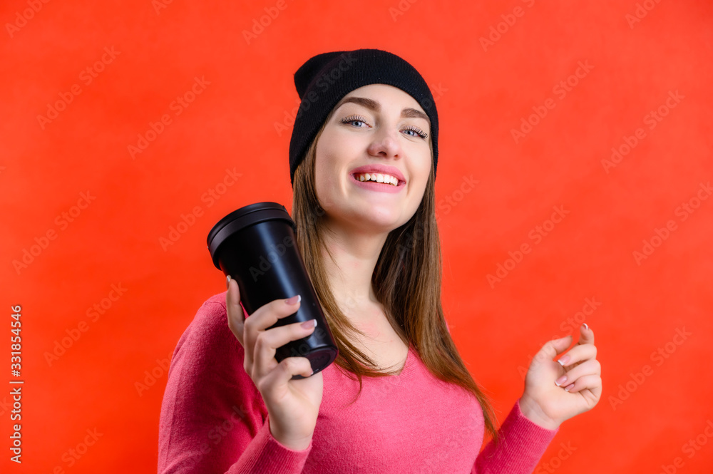 Portrait of a pretty smiling Caucasian woman in a pink sweater on a red background. The model stands in front of the camera in a black hat with different emotions. Portrait of a pretty smiling Caucasian woman in a pink sweater on a red background. The model stands in front of the camera in a black hat with different emotions.