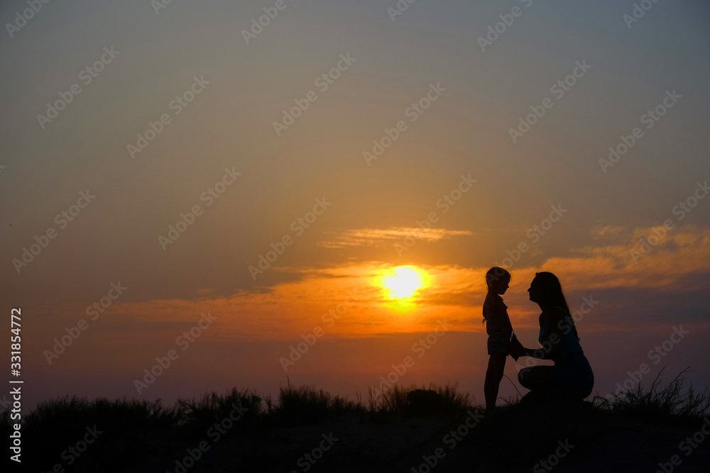 Silhouettes of mother and little daughter at sunset.