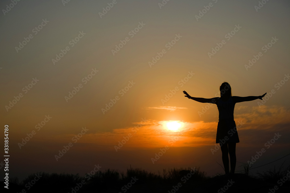 Silhouette of a girl on top of a mountain at sunset.