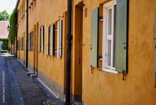Mustard yellow walls and green shuttered windows of the Fuggerei. The Fuggerei is the world's oldest social housing complex still in use. It is a walled enclave. 