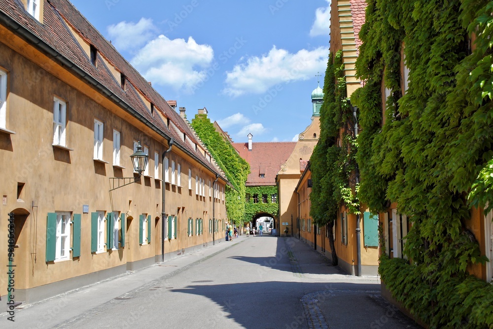 Augsburg, Germany - 2015: Mustard stucco walls, vine covered buildings and neat streets in the Fuggerei, the world's oldest social housing complex still in use. It is a walled enclave. 