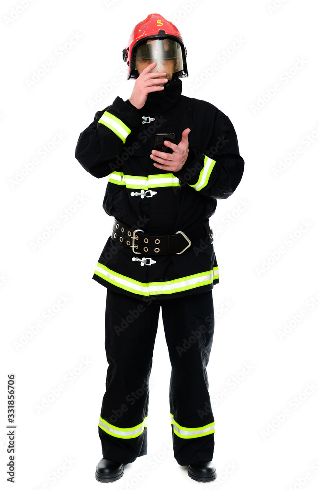 Portrait of a fireman with a phone in his hands in a black uniform in a red helmet on a white isolated background Portrait of a fireman with a phone in his hands in a black uniform in a red helmet on a white isolated background