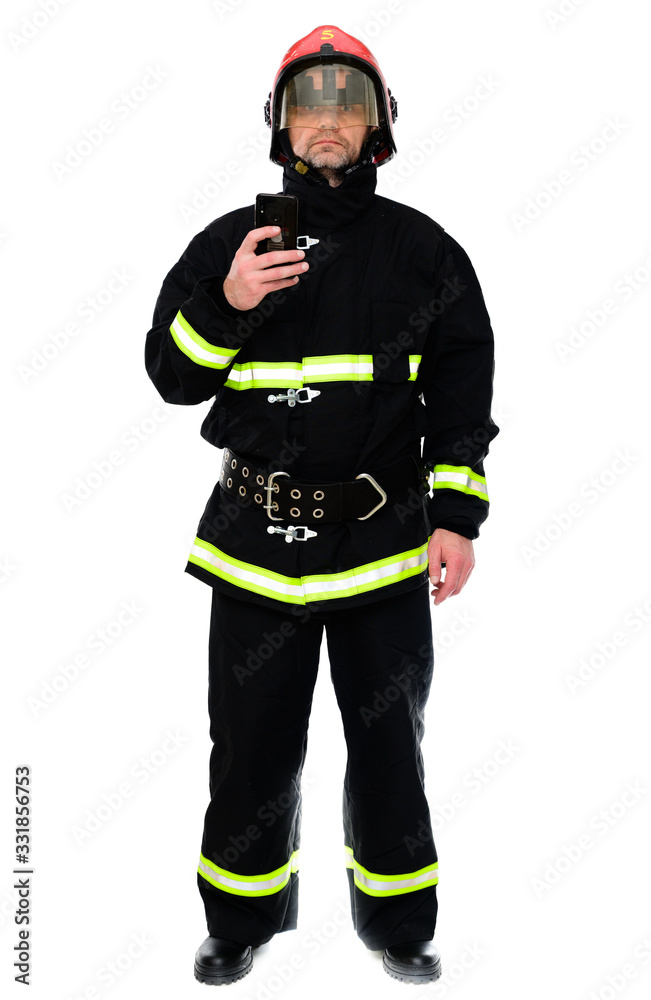Naklejka premium Portrait of a fireman with a phone in his hands in a black uniform in a red helmet on a white isolated background