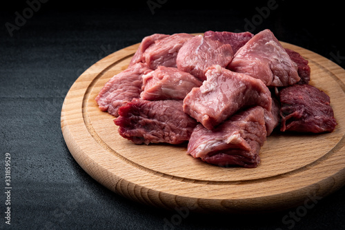 Raw pork sliced meat on wooden board on black background.