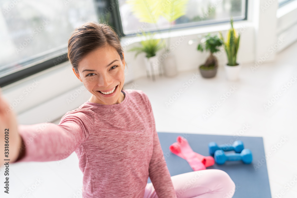 Happy selfie at home Asian young woman smiling training bodyweight exercises on exercise mat in living room of apartment taking mobile phone photo during workout. Happy selfie at home Asian young woman smiling training bodyweight exercises on exercise mat in living room of apartment taking mobile phone photo during workout.