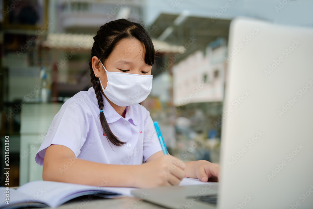 social distancing concept, Junior Primary school girl Do homework at home with laptop. the school is closed during an outbreak of the Coronavirus Covid-19 and Dust PM2.5 in Bangkok Thailand asia social distancing concept, Junior Primary school girl Do homework at home with laptop. the school is closed during an outbreak of the Coronavirus Covid-19 and Dust PM2.5 in Bangkok Thailand asia
