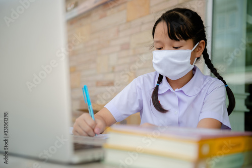 social distancing concept, Junior Primary school girl Do homework at home with laptop. the school is closed during an outbreak of the Coronavirus Covid-19 and Dust PM2.5 in Bangkok Thailand asia 