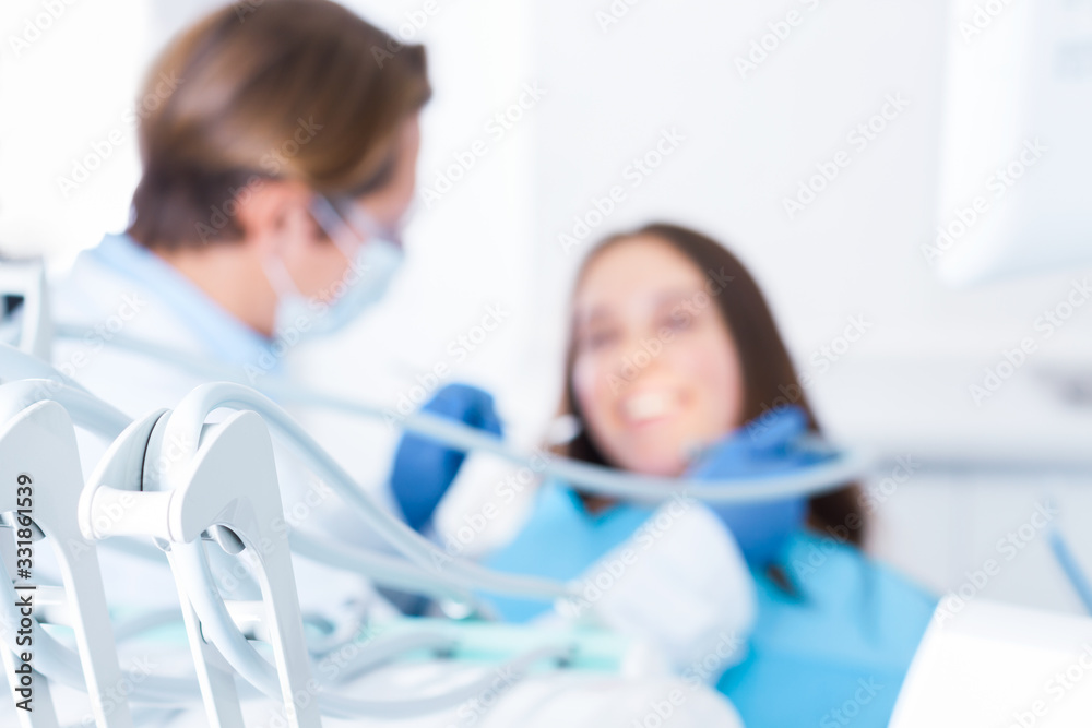 Fototapeta premium Closeup of dental tools, instruments. On background young smiling woman is sitting in blue chair in clinic, office. Man doctor is conducting examination of teeth. Visit to dentist concept.