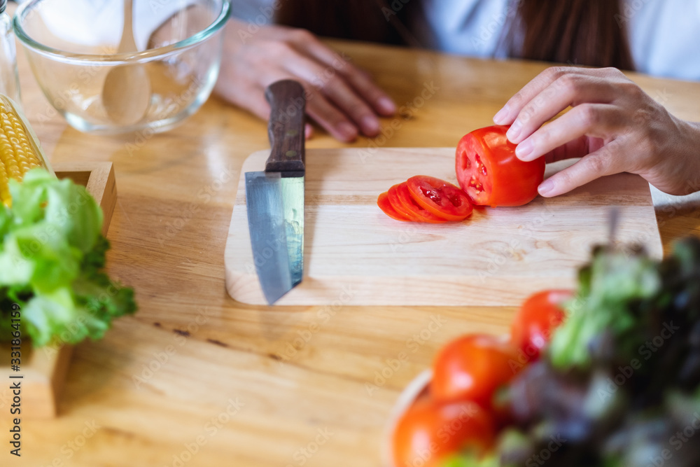Closeup image of a woman chef looking and cutting tomato by knife on wooden board Closeup image of a woman chef looking and cutting tomato by knife on wooden board