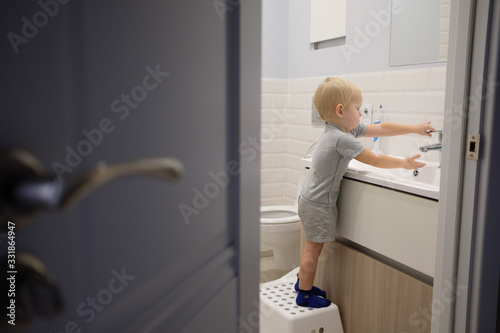 Fototapeta Little blond boy learning brushing his teeth in bath