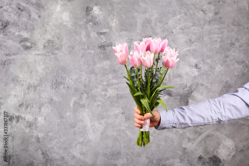 Studio shot of young man wearing cotton shirt, holding beautiful bouquet of pink flowers. Close up, copy space, background.