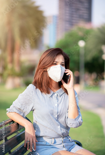 Adult Asian WomanSitting in Public Park. She Wearing Virus Protective Mask in Prevention for Coronavirus or Covid-19 Outbreak Situation - Healthcare and Lifestyle Concept photo