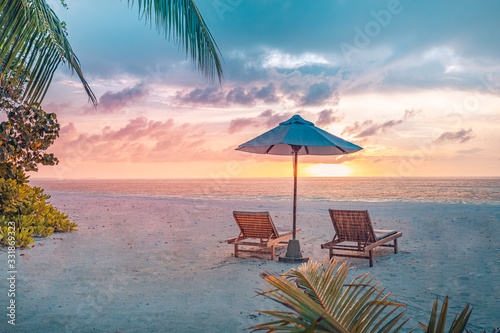 Luxury tropical sunset scenery, two sun beds, loungers, umbrella under palm tree. White sand, sea view with horizon, colorful twilight sky, calmness and relaxation. Vacation beach resort hotel © icemanphotos