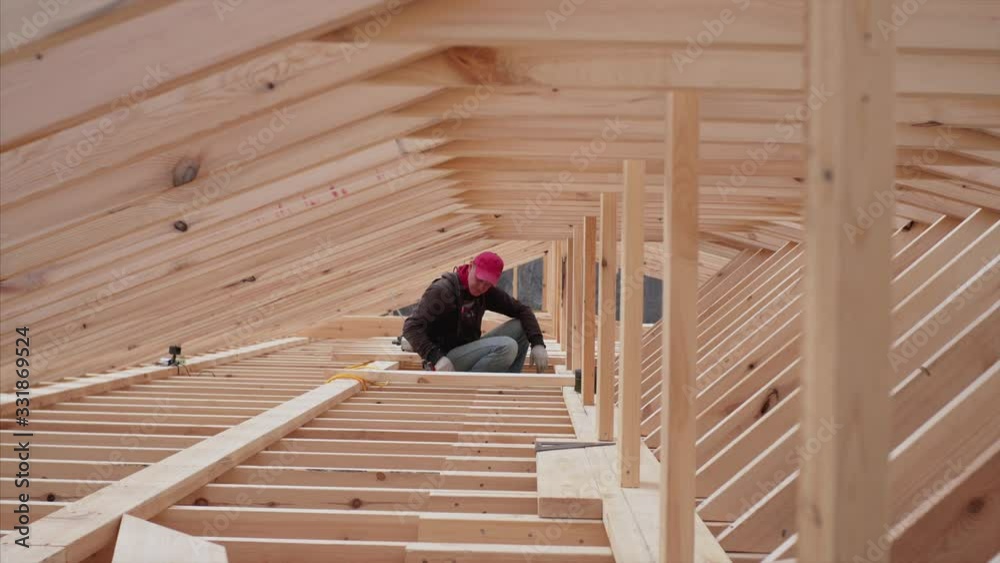Builder in attic is taking and passing to someone on the roof wooden planks. Frame house under construction Builder in attic is taking and passing to someone on the roof wooden planks. Frame house under construction