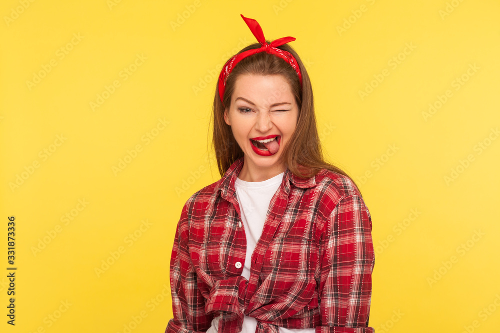 Portrait of optimistic pinup girl in checkered shirt and headband winking to camera with crazy naughty expression Portrait of optimistic pinup girl in checkered shirt and headband winking to camera with crazy naughty expression