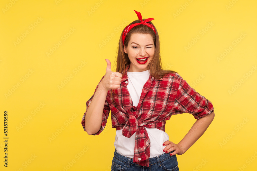 Good job, like it! Portrait of happy coquette pinup girl in checkered shirt winking to camera and showing thumbs up Good job, like it! Portrait of happy coquette pinup girl in checkered shirt winking to camera and showing thumbs up