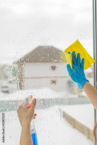 Hands in the blue gloves wash window with spray