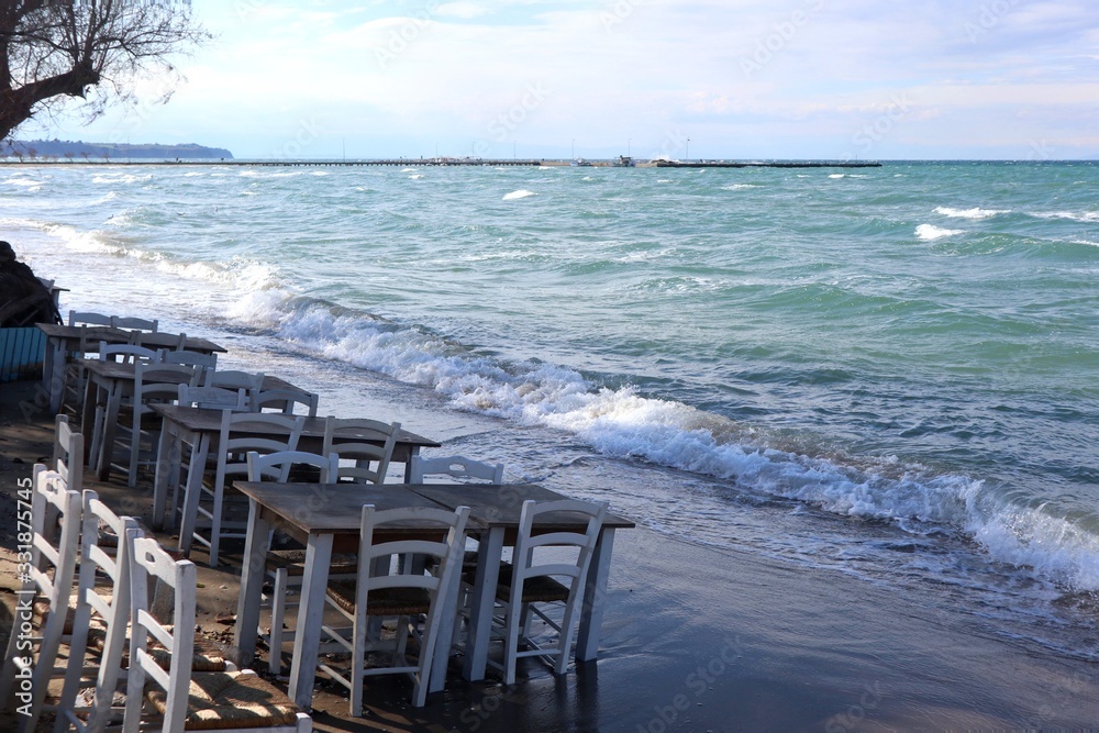 White chairs and tables on the beach. Windy day by the blue sea. White chairs and tables on the beach. Windy day by the blue sea.