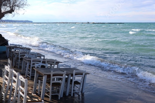 White chairs and tables on the beach. Windy day by the blue sea.
