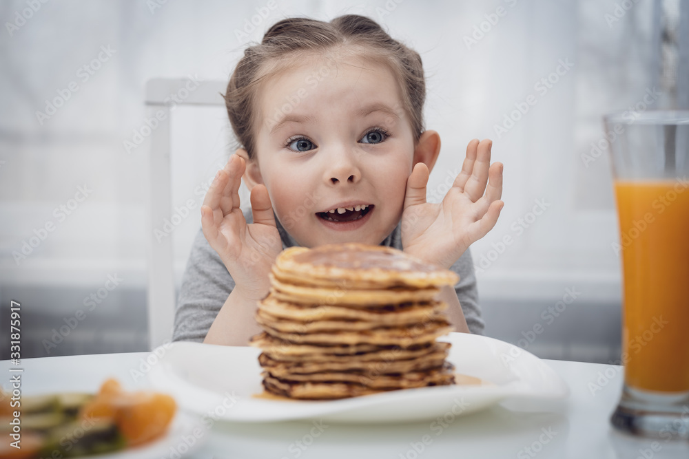 Selected focus. Little girl looking at homemade pancakes with honey on table Selected focus. Little girl looking at homemade pancakes with honey on table