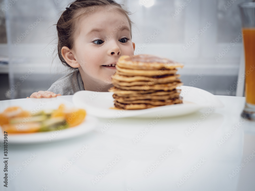 Selected focus. Little girl looking at homemade pancakes with honey on table Selected focus. Little girl looking at homemade pancakes with honey on table