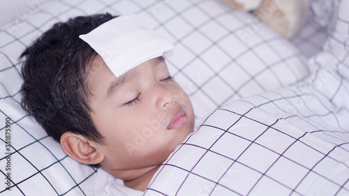 Asian 2-3  years old toddler boy child gets high fever lying on bed with cold compress, wet washcloth on forehead to relieve pain, cool a fever, Cold, Flu Treatment in Children, Home Remedies concept