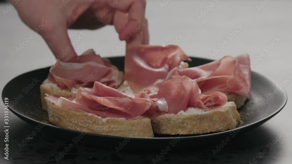 Slow motion man hand take bruschetta with prosciutto and ricotta from black plate Slow motion man hand take bruschetta with prosciutto and ricotta from black plate