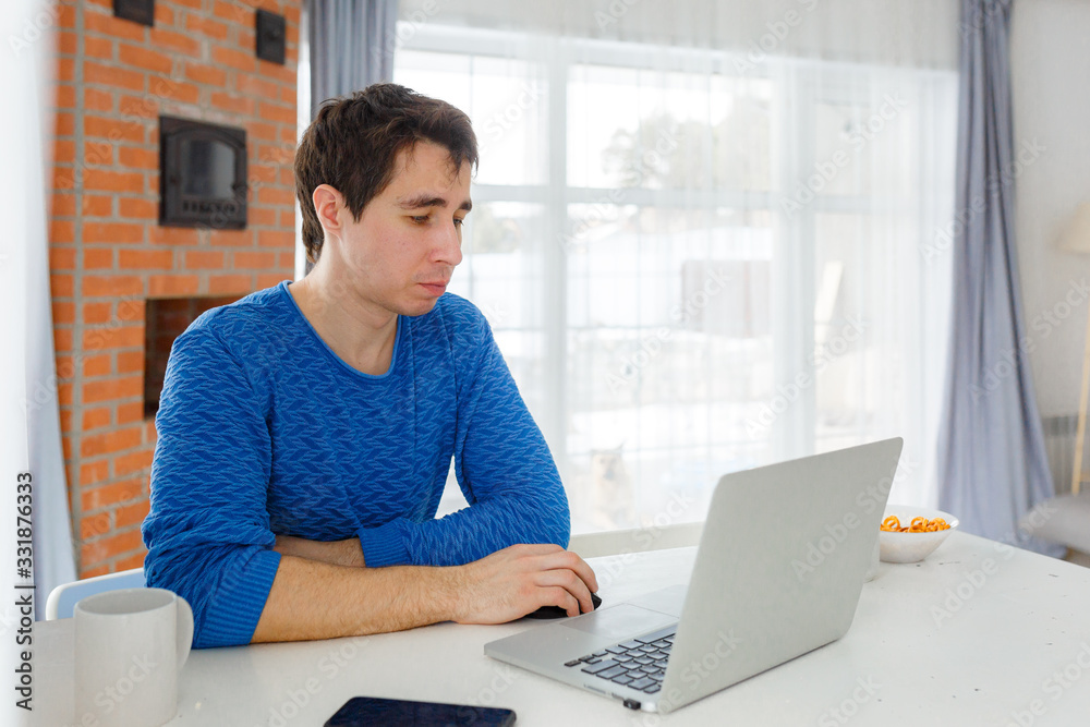 young attractive man freelancer working at home on a computer at the bright kitchen, stay at home young attractive man freelancer working at home on a computer at the bright kitchen, stay at home