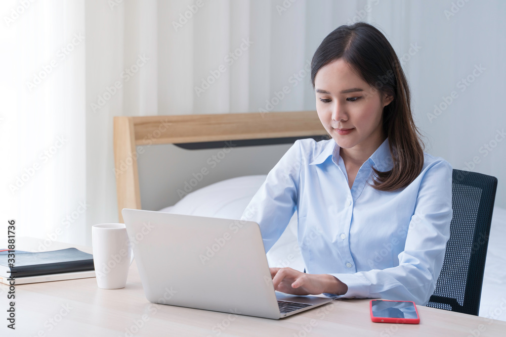 Attractive Asian woman works from home with laptop on desk in bedroom. Young girl smiling with happiness face while reading at computer screen. Telecomuting, freelancer and modern lifestyle concept. Attractive Asian woman works from home with laptop on desk in bedroom. Young girl smiling with happiness face while reading at computer screen. Telecomuting, freelancer and modern lifestyle concept.