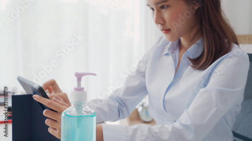 Selective focus of alcohol gel bottle on table  woman working in blur background prepared sanitizer gel for hand wash to clean germ  bacteria and virus. Pandemic protection and Health care concept.