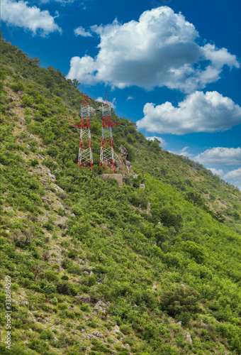 Red and white high power pylons on a steep green hill