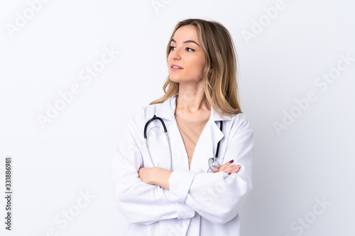Young woman over isolated white background wearing a doctor gown and with arms crossed looking side