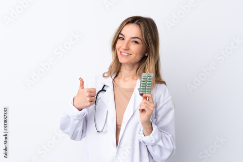 Young woman over isolated white background wearing a doctor gown and holding pills