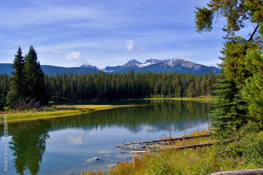 Beautiful lake high in the mountains surrounded by forest. Blue sky, white clouds. Canadian Rockies.