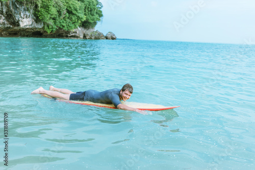 A young male surfer rowing on a surfboard in the Indian ocean, near the beach.
