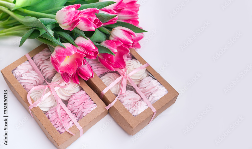 A box of sweets and a bouquet of flowers on a white background. Homemade marshmallows and tulips A box of sweets and a bouquet of flowers on a white background. Homemade marshmallows and tulips