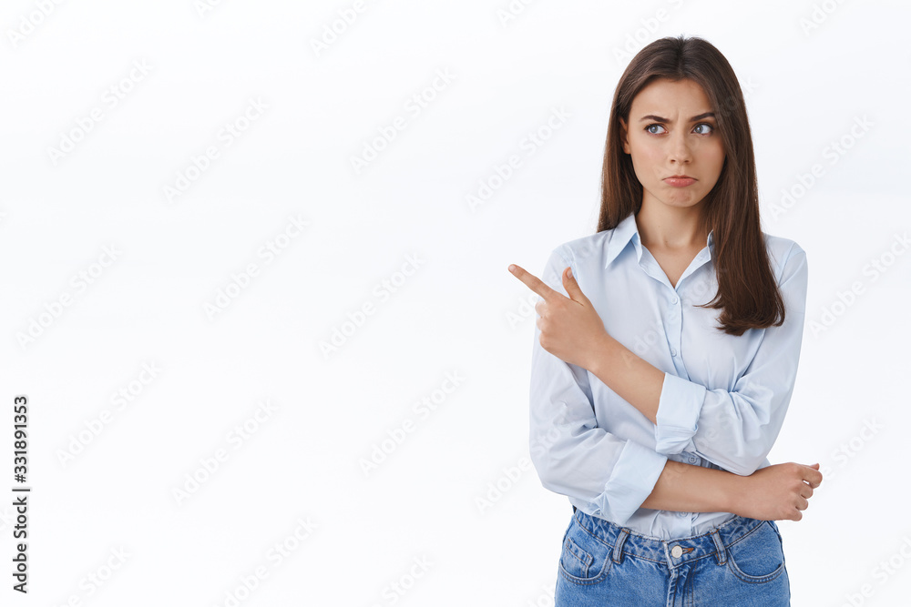 Doubtful and unsure businesswoman looking skeptical with slight disblief, pouting thoughtful while pointing finger left at strangely good offer, hesitating and pondering white background Doubtful and unsure businesswoman looking skeptical with slight disblief, pouting thoughtful while pointing finger left at strangely good offer, hesitating and pondering white background