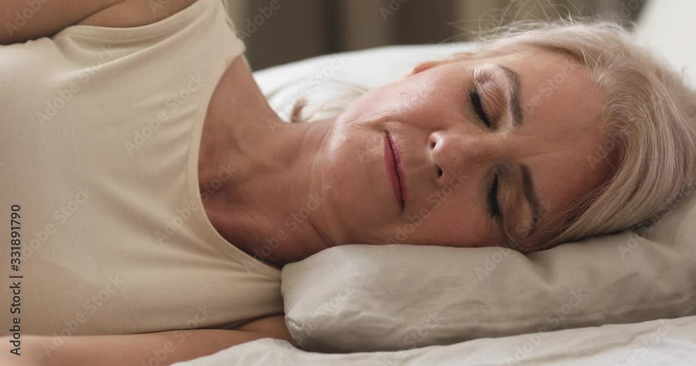 Head shot close up carefree mature older granny sleeping on orthopedic pillow mattress, resting in holiday weekend morning. Calm happy middle aged mature woman seeing sweet dreams at home or hotel. Head shot close up carefree mature older granny sleeping on orthopedic pillow mattress, resting in holiday weekend morning. Calm happy middle aged mature woman seeing sweet dreams at home or hotel.