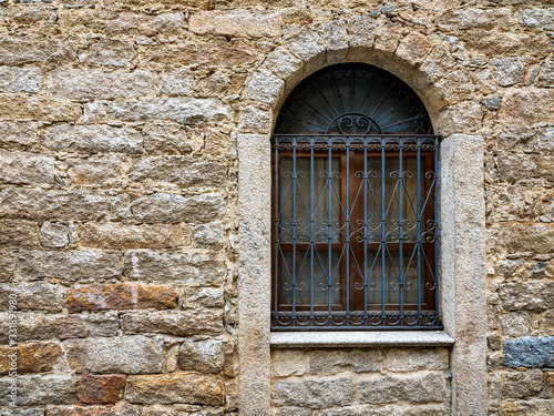 Arched window with wrought iron grate and ancient wall built with stones of various types and thickness