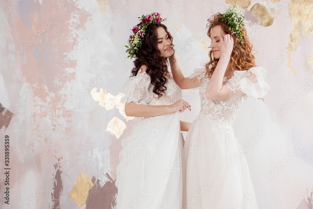 Two charming brides in beautiful spring wreaths on their heads. Beautiful young women in wedding dresses Two charming brides in beautiful spring wreaths on their heads. Beautiful young women in wedding dresses