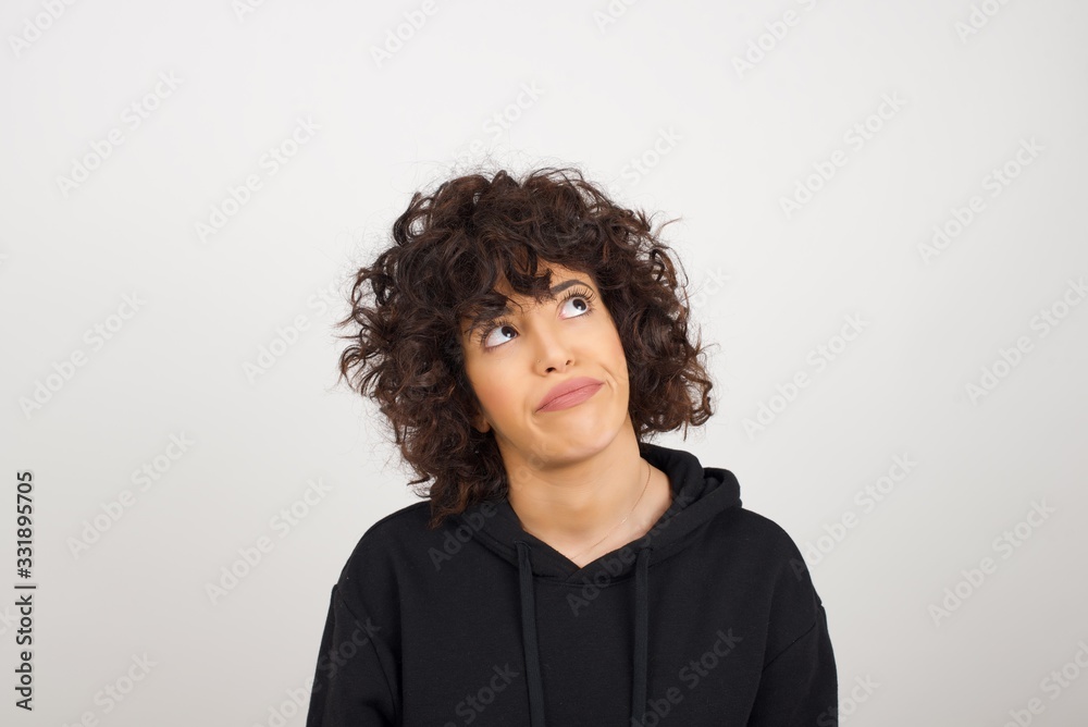 Gloomy, wondering young woman looking up with lips together, being upset thinking about something important, keeps hands down. Gloomy, wondering young woman looking up with lips together, being upset thinking about something important, keeps hands down.