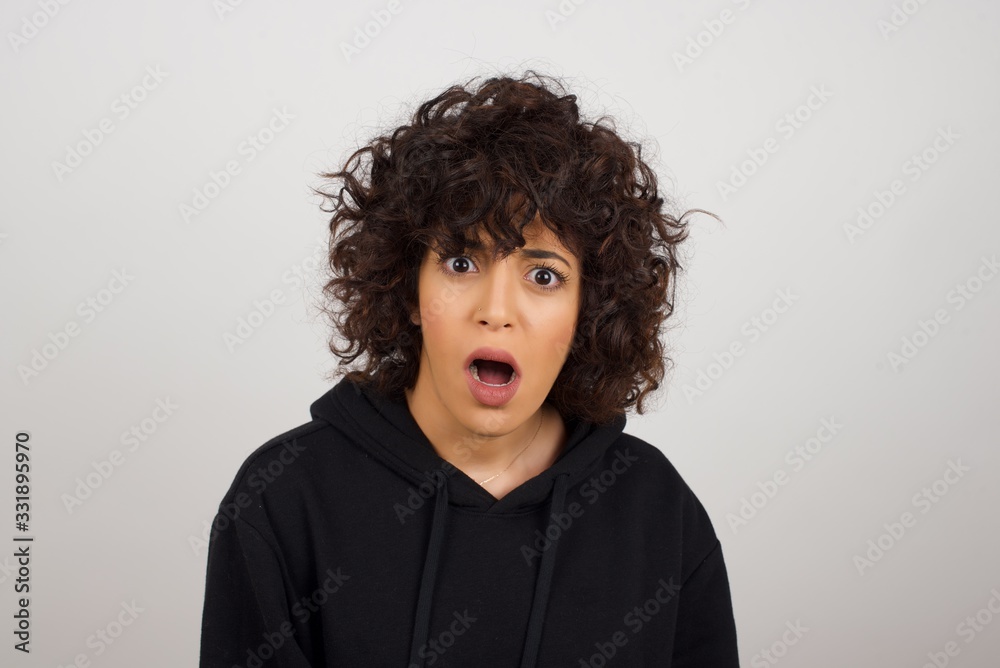 Expressive facial expressions. Shocked stupefied female, keeps jaw dropped, feels stunned from what she sees aside on blank gray Wall Expressive facial expressions. Shocked stupefied female, keeps jaw dropped, feels stunned from what she sees aside on blank gray Wall