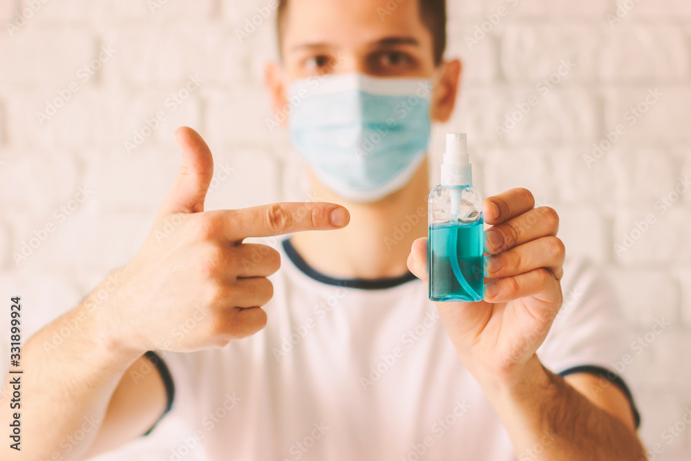 Closeup of confident doctor pointing with finger on sanitizer bottle as preventive measure against coronavirus COVID-19, nCov-19. Young man holding and showing antibacterial gel dispenser in hand Closeup of confident doctor pointing with finger on sanitizer bottle as preventive measure against coronavirus COVID-19, nCov-19. Young man holding and showing antibacterial gel dispenser in hand