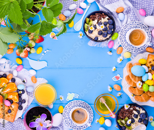 Easter breakfast scene shot from above. Cups for tea, cake with jam, cookies, fresh orange juice, fruits, granola with berries, honey, strawberries with leaves and berries