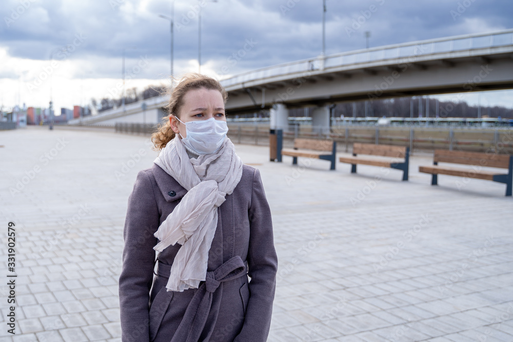 young European woman in protective disposable medical mask walking  in deserted city street outdoor. concept of coronavirus influenza covid-19 quarantine and people panic