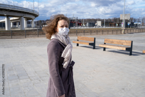 young European woman in protective disposable medical mask walking in deserted city street outdoor. concept of coronavirus influenza covid-19 quarantine and people panic