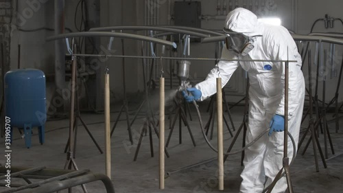 Varnishing of wooden parts. A man in a protective suit sprays powder paint from a gun