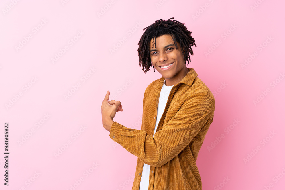Young African American man with corduroy jacket over isolated pink background pointing back Young African American man with corduroy jacket over isolated pink background pointing back