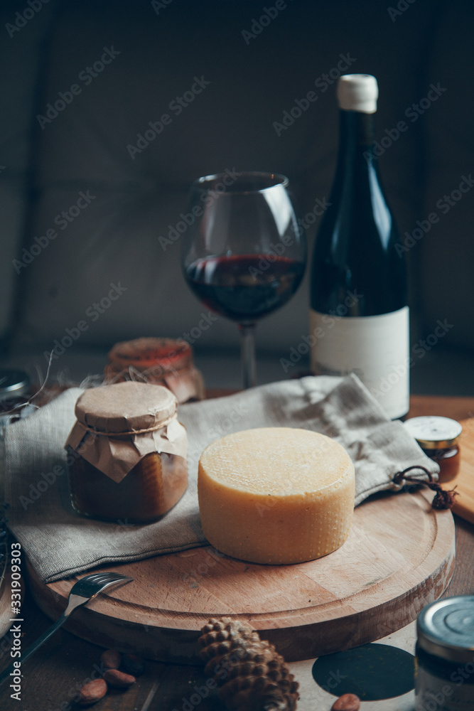 A smooth circle of hard cheese with wine and a glass. Farm cheeses on a wooden Board. Still life with hard sliced cheese. A smooth circle of hard cheese with wine and a glass. Farm cheeses on a wooden Board. Still life with hard sliced cheese.