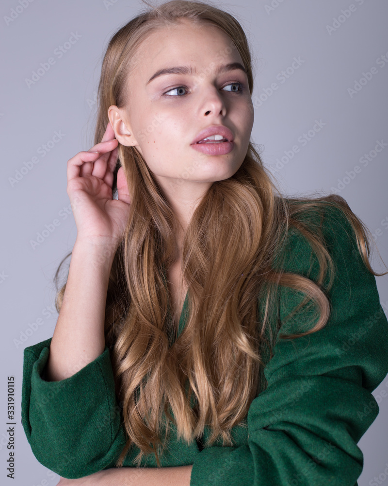 An image of an attractive, elegant blonde standing in a green coat An image of an attractive, elegant blonde standing in a green coat